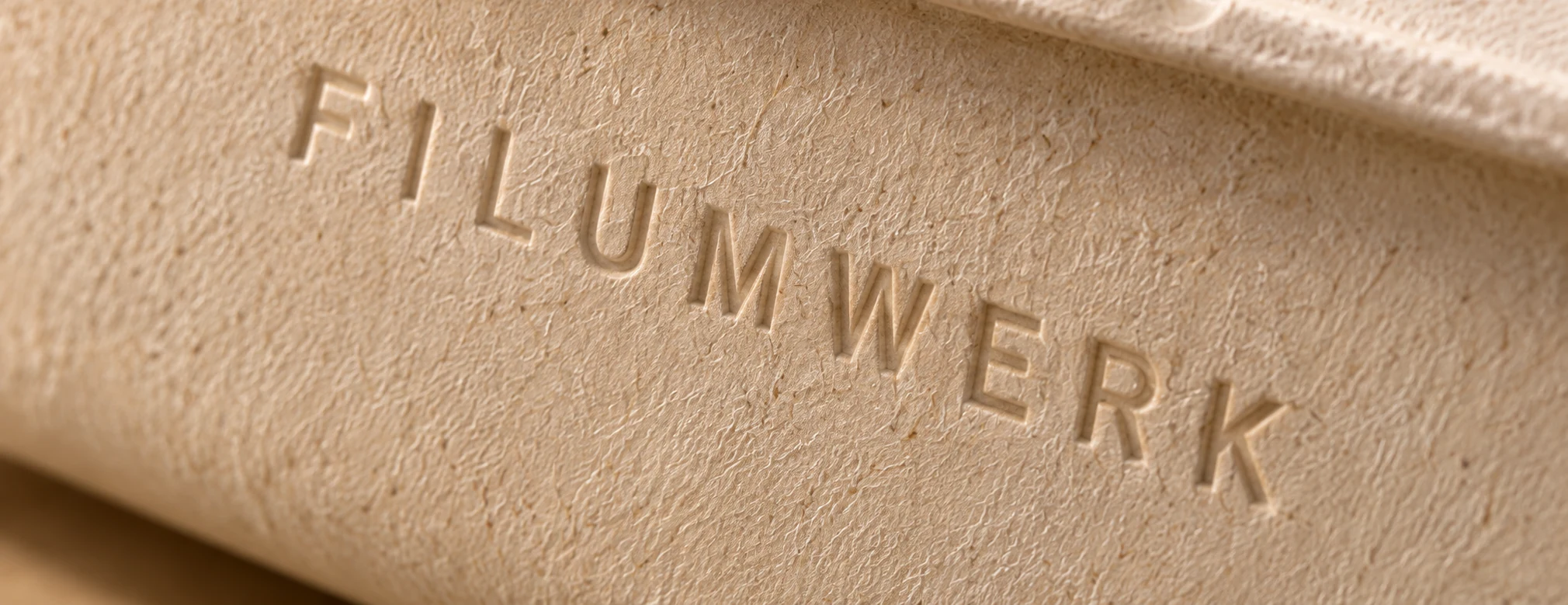 Close-up of the FILUMWERK wordmark embossed into moulded fibre packaging.